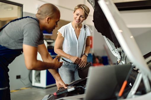 Happy Woman Talking To Her Car Mechanic In A Repair Shop.